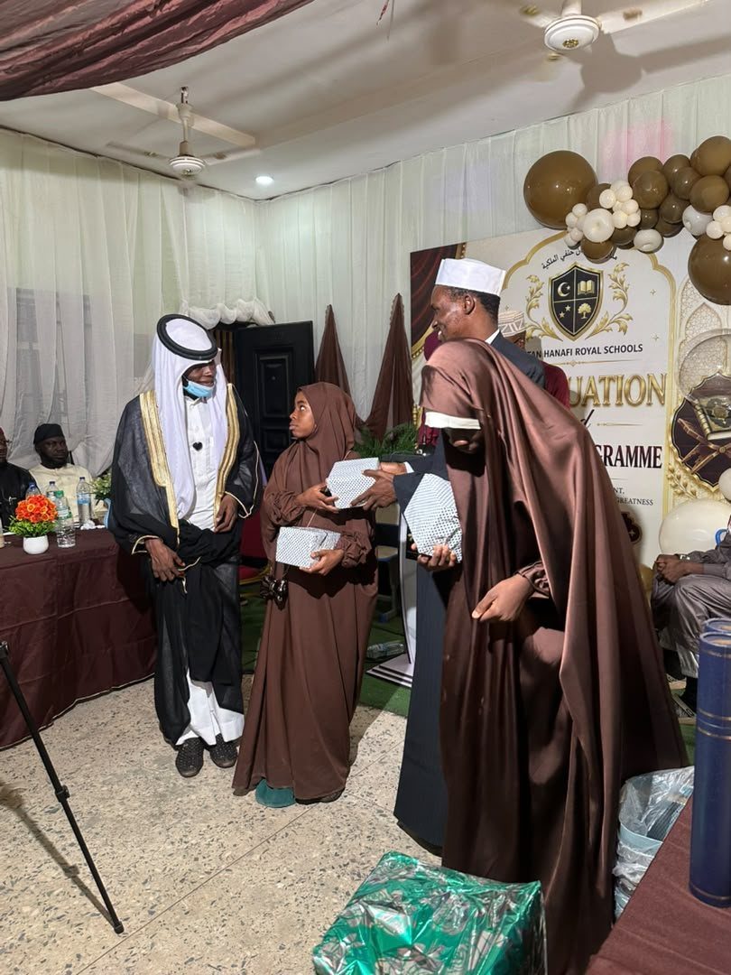 A Hifz graduand receiving her prizes from a member of the faculty at the graduation ceremony, with a visiting scholar standing alongside